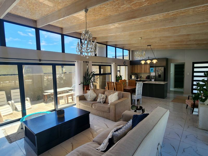 Spacious open-plan living and kitchen area featuring high exposed timber beam ceilings, large format tiled flooring, and extensive glass doors leading to the patio.