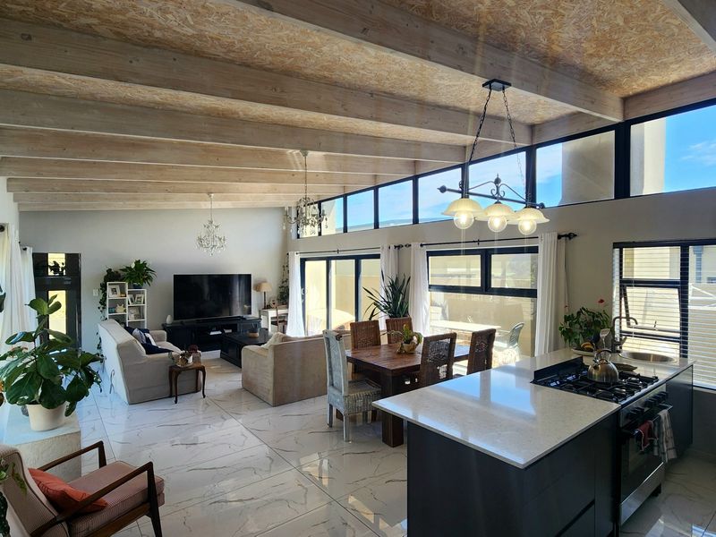 Spacious open-plan living area featuring high exposed timber beam ceilings, modern marble-look flooring, and a contemporary kitchen with a central island and gas hob.
