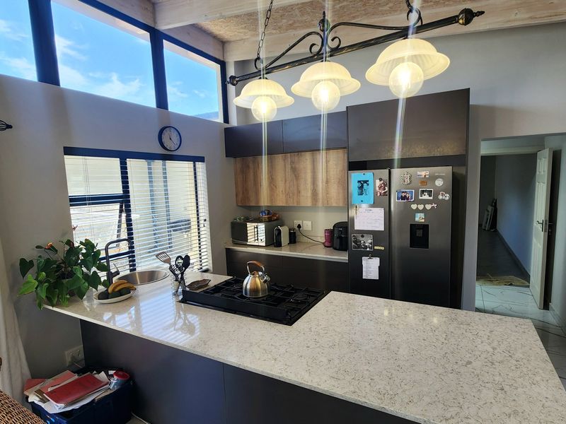 Modern kitchen featuring a central island with a gas hob, stone countertops, sleek cabinetry, and high-level windows that provide ample natural light.