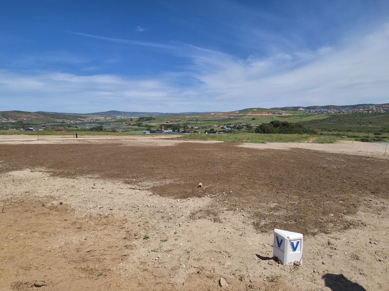 A vacant residential plot featuring a utility connection point, offering expansive views of the surrounding landscape and neighborhood.