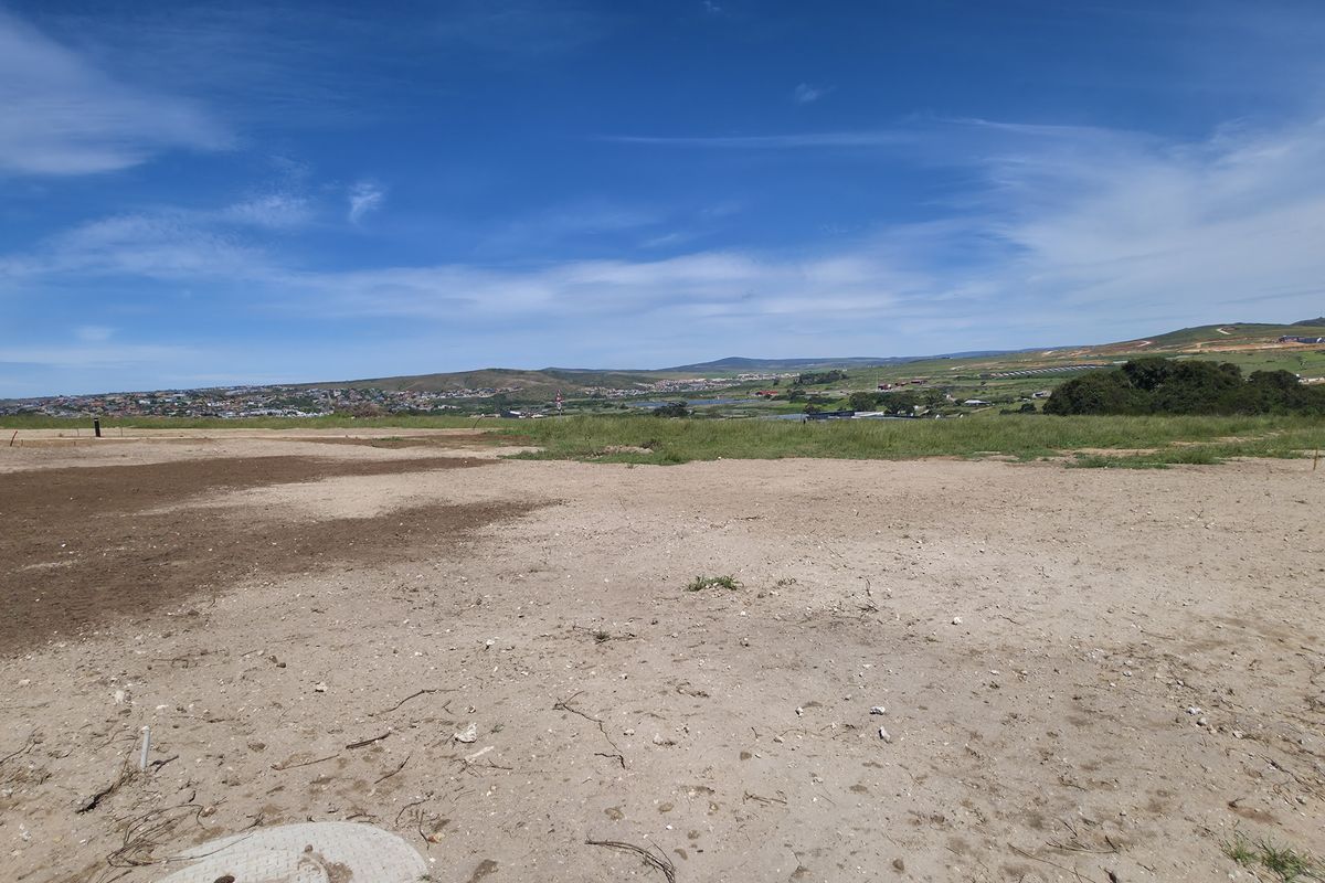 A vacant residential plot featuring level ground and direct access to a paved road, offering expansive views of the surrounding landscape.