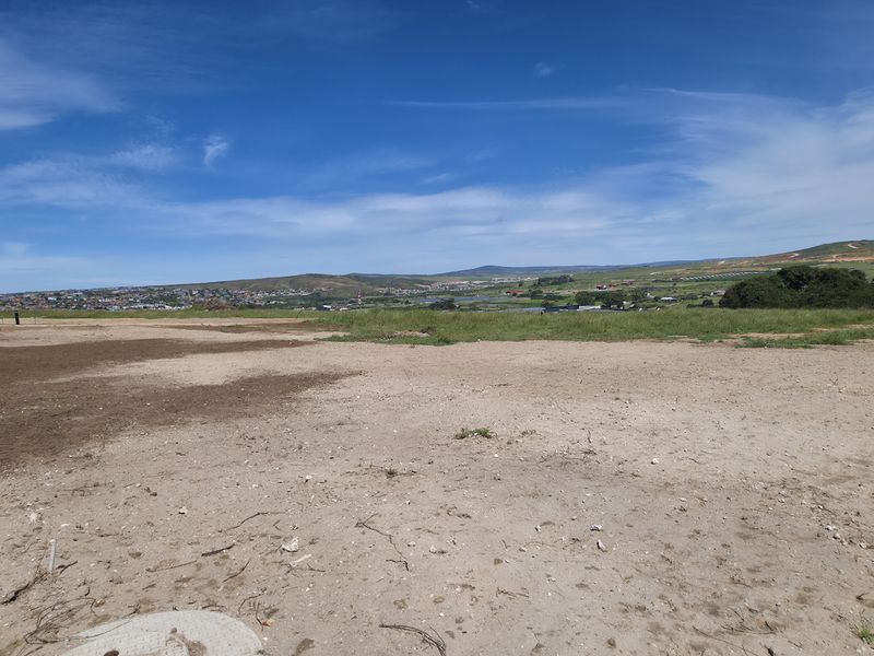 A vacant residential plot featuring level ground and direct access to a paved road, offering expansive views of the surrounding landscape.