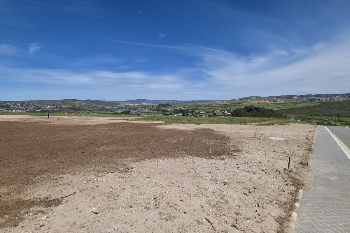 A vacant residential plot featuring a level building site, adjacent to a paved road and sidewalk, offering expansive views of the surrounding landscape.