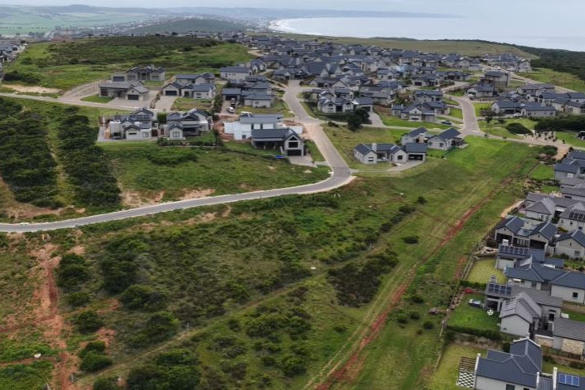 An aerial view of a residential estate development featuring paved roads and established homes with coastal views in the background.