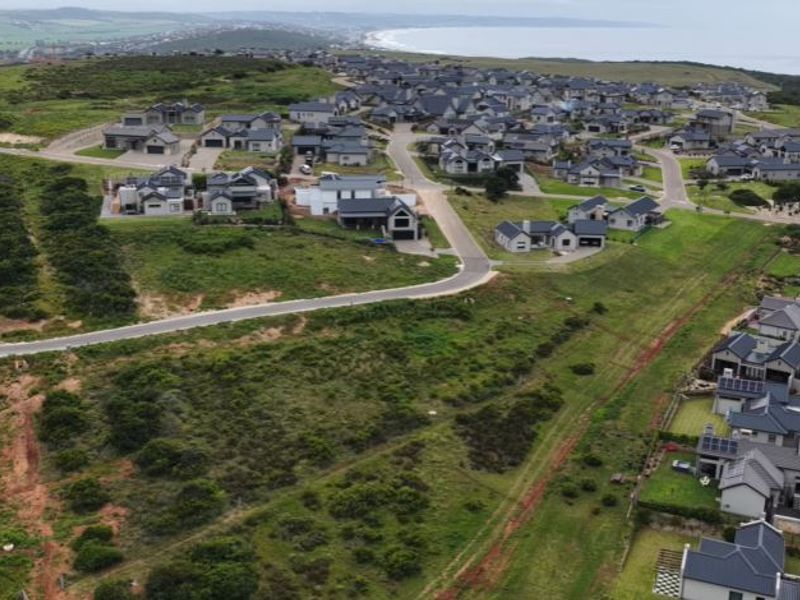 An aerial view of a residential estate development featuring paved roads and established homes with coastal views in the background.