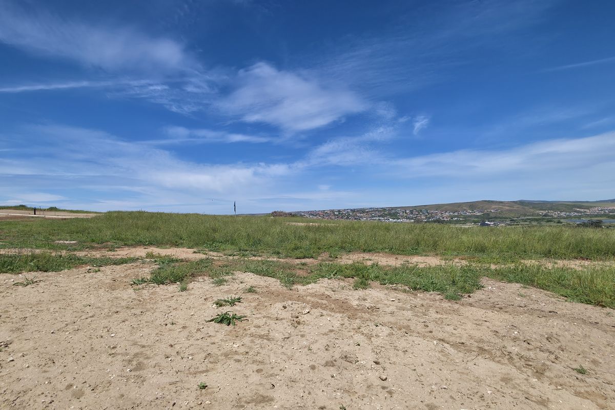 A wide-angle view of a vacant residential plot featuring natural terrain and distant landscape vistas under a clear blue sky.
