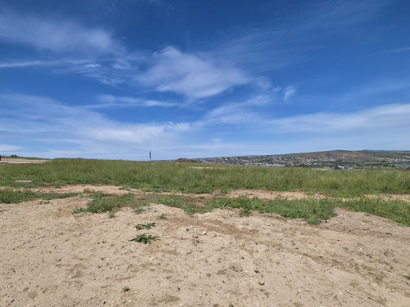 A wide-angle view of a vacant residential plot featuring natural terrain and distant landscape vistas under a clear blue sky.