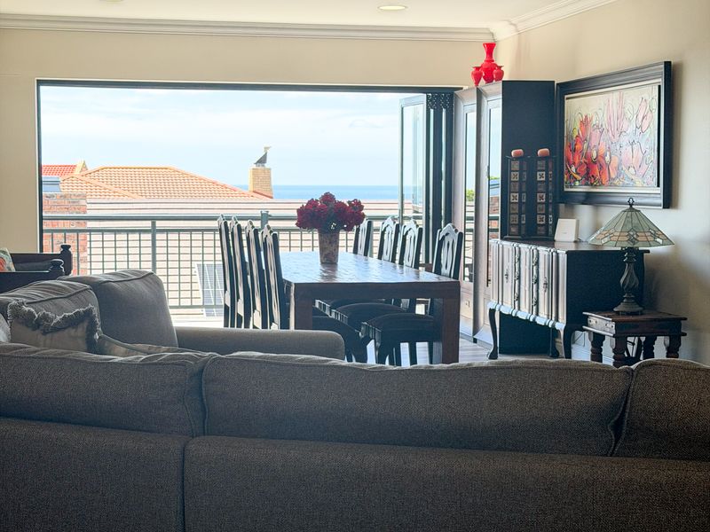 Spacious open-plan living and dining area featuring recessed lighting and large bi-fold doors opening to a balcony with ocean views.