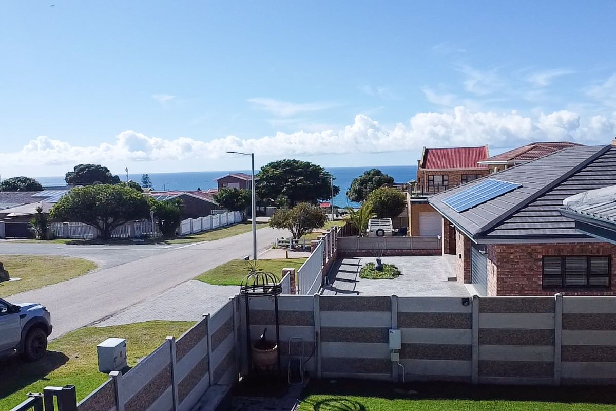Elevated view overlooking a residential street and neighbourhood with a distant sea view and visible solar panels on the roof.