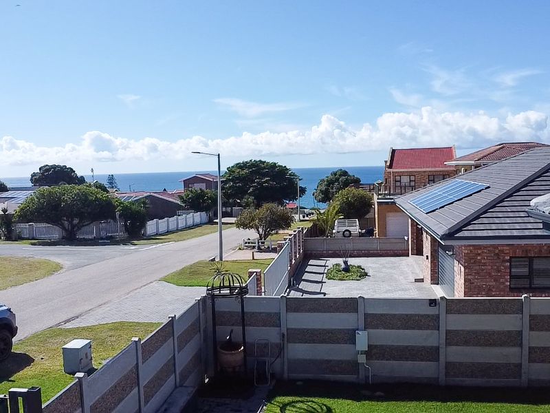Elevated view overlooking a residential street and neighbourhood with a distant sea view and visible solar panels on the roof.