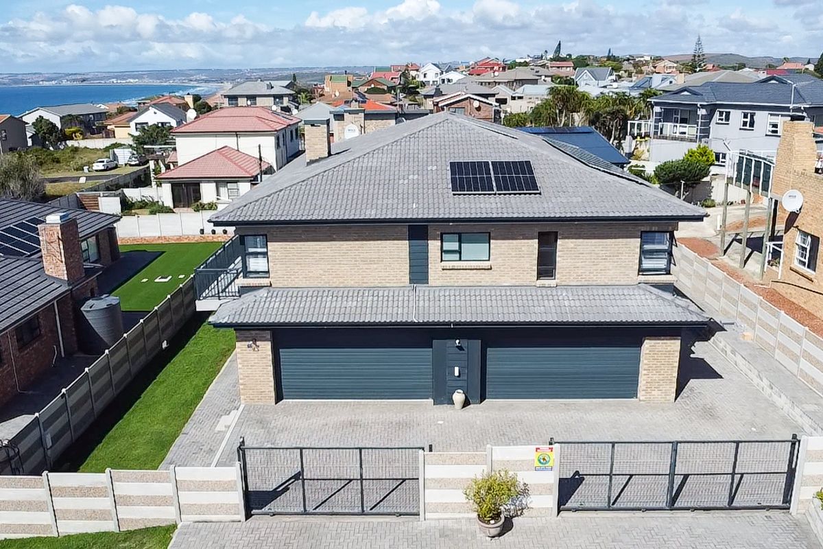 Aerial view of a modern double-story brick house featuring a tiled roof, solar panels, a double garage, and a secure paved driveway.