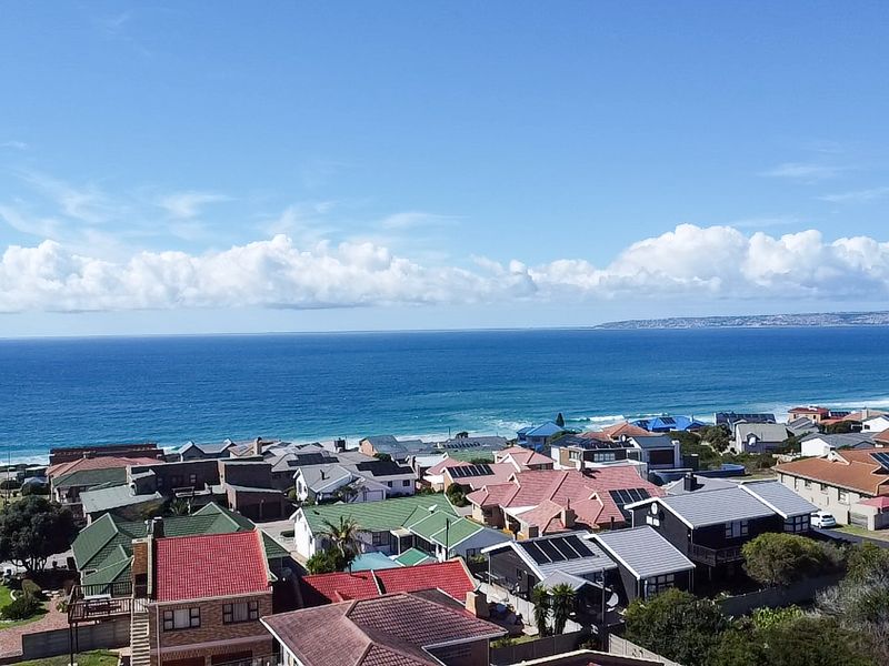 An elevated aerial view overlooking a coastal residential neighborhood with clear ocean vistas and blue skies.