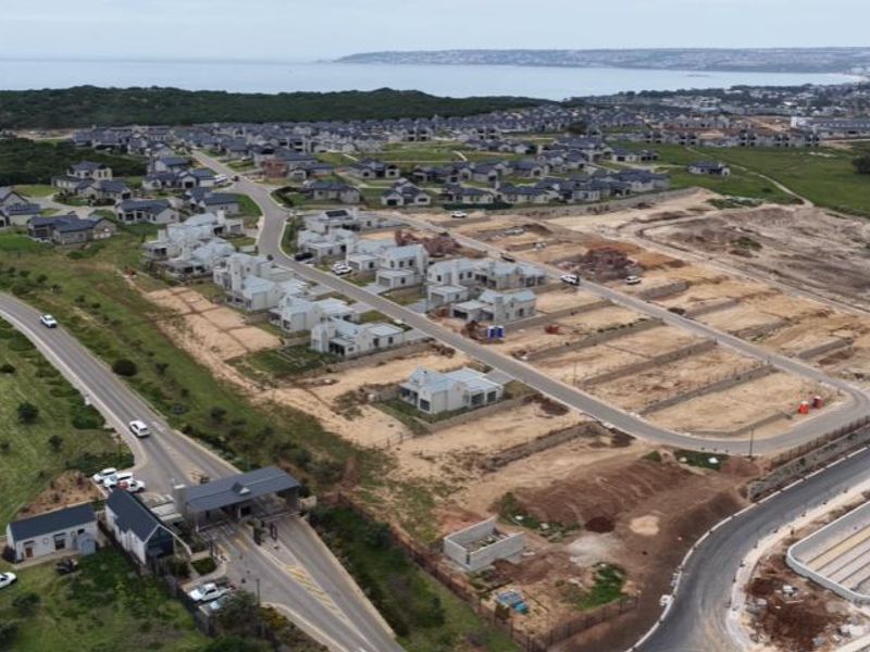 Aerial view of a developing residential estate featuring paved roads, a security gatehouse, and multiple vacant plots ready for construction.