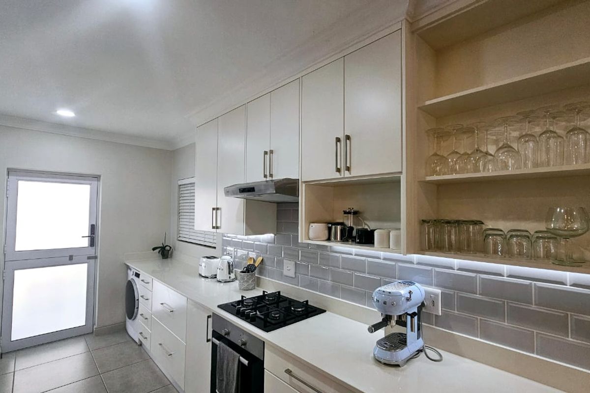 Modern kitchen featuring white cabinetry, stone countertops, subway tile backsplash, built-in gas cooktop, oven, and integrated laundry facilities with under-cabinet lighting.