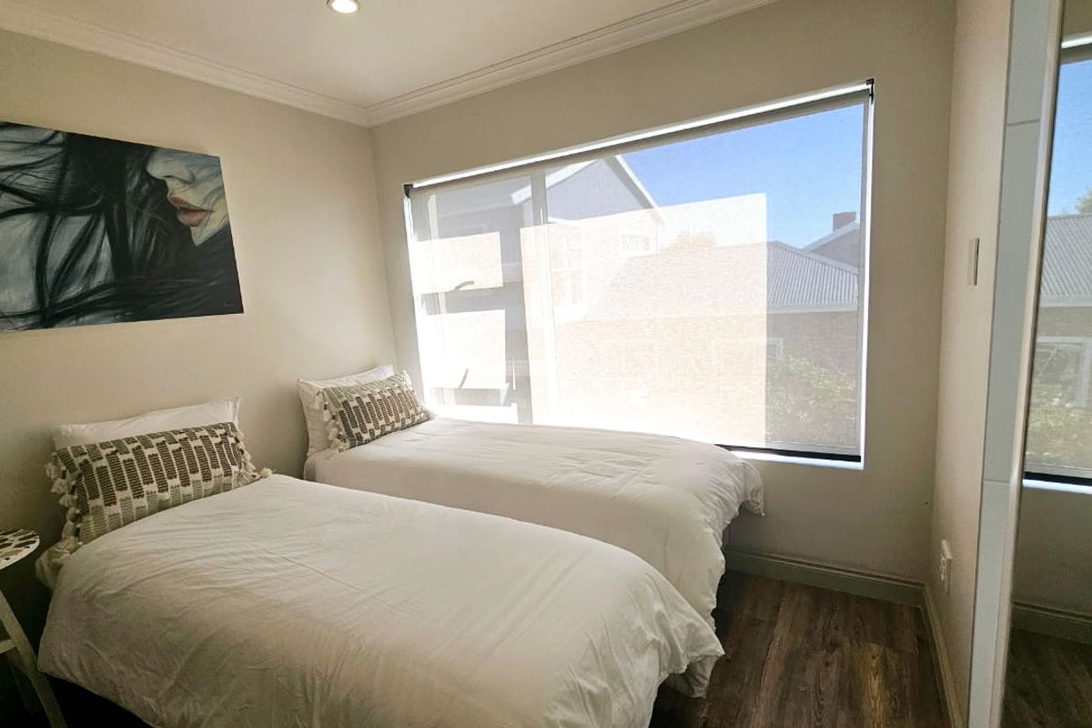 A bright and well-maintained bedroom featuring laminate flooring, large windows with roller blinds, and modern recessed downlighting.