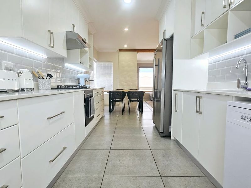 Modern galley-style kitchen featuring white cabinetry, stone countertops, subway tile backsplash, integrated appliances, and sleek under-cabinet lighting.