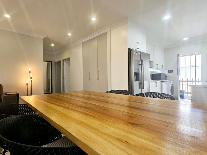 A bright open-plan living and kitchen area featuring modern cabinetry, recessed lighting, and a seamless flow between the dining space and kitchen.