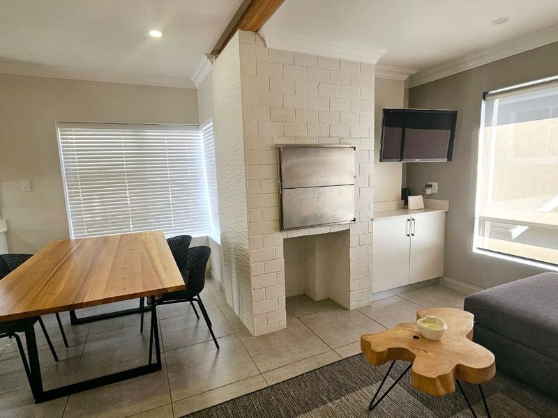 Open-plan living and dining area featuring a central white brick built-in braai, tiled flooring, and modern cabinetry with integrated lighting.