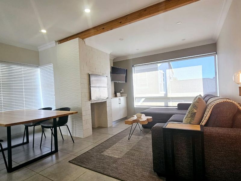 Open-plan living and dining area featuring tiled floors, a built-in fireplace with textured surround, and an exposed timber ceiling beam.