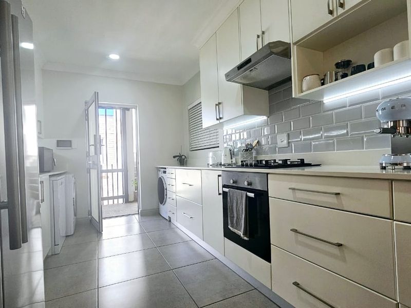 Modern kitchen featuring sleek cabinetry, subway tile backsplash, integrated gas hob, built-in oven, and tiled flooring with direct access to an outdoor area.