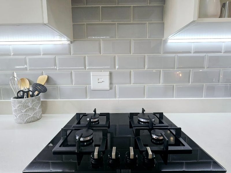 Modern kitchen featuring a sleek black gas hob, white quartz countertops, and a stylish grey subway tile backsplash with integrated under-cabinet lighting.