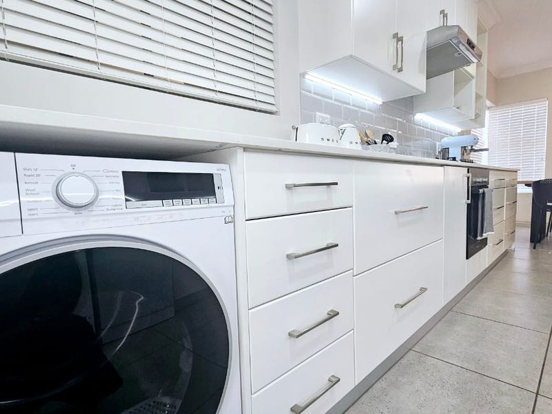 Modern kitchen featuring white cabinetry, built-in oven, extractor fan, tiled backsplash, and under-cabinet lighting with neutral tiled flooring.