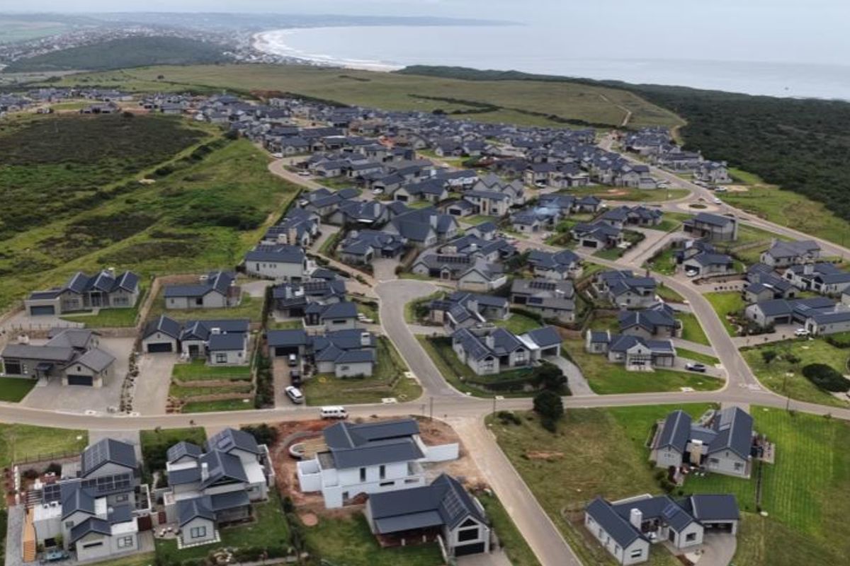An aerial view of a residential estate featuring multiple homes, paved streets, and proximity to the coastline.