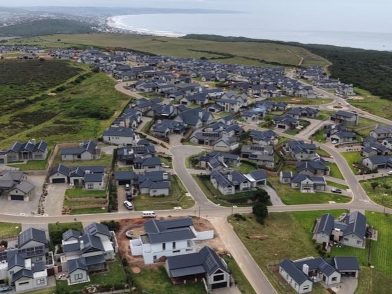 An aerial view of a residential estate featuring multiple homes, paved streets, and proximity to the coastline.