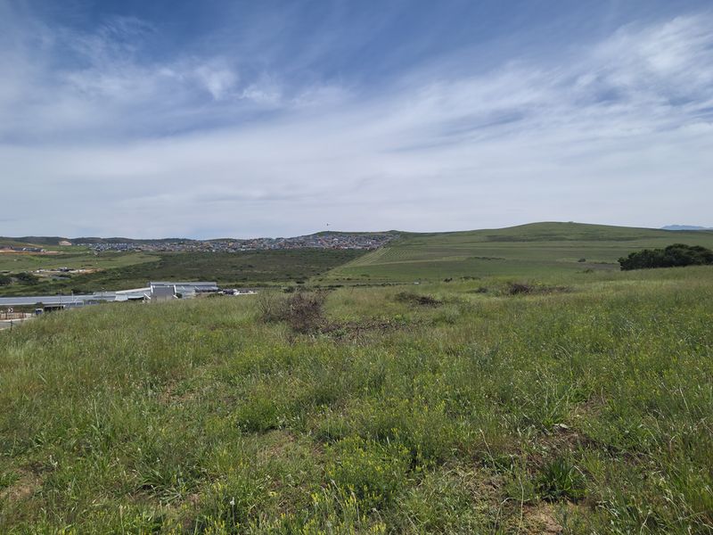 A wide-angle view of the vacant residential land, showcasing the surrounding landscape, natural vegetation, and nearby paved road access.