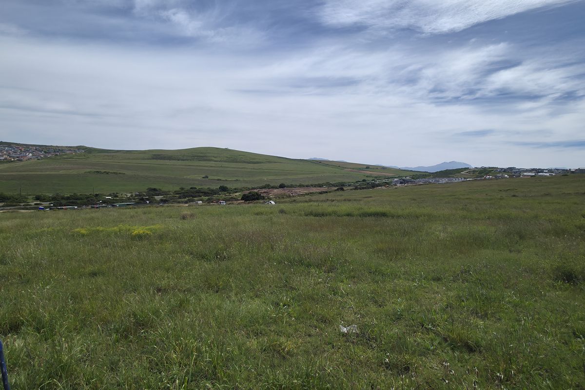 A wide-angle view of an expansive, undeveloped residential plot featuring natural grassland with surrounding hills and distant neighborhood scenery.