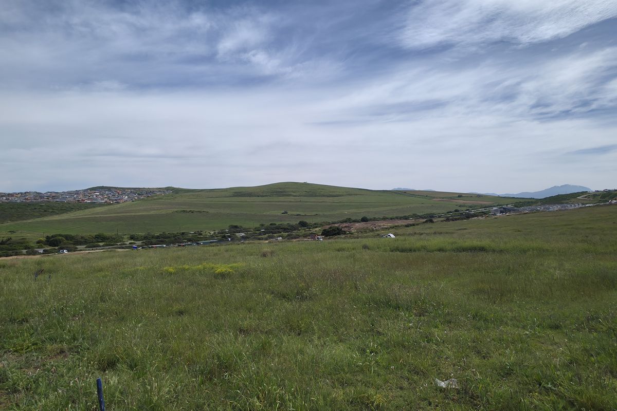 A wide-angle view of an expansive, undeveloped residential plot featuring natural grassland and distant hillside scenery.