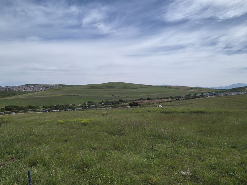 A wide-angle view of an expansive, undeveloped residential plot featuring natural grassland and distant hillside scenery.