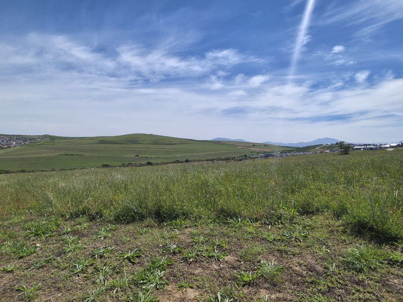 A wide-angle view of the vacant residential land, showcasing the surrounding landscape and distant hillside terrain.
