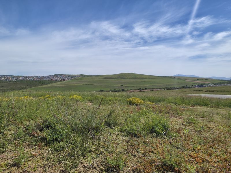 A wide-angle view of the vacant residential land, showcasing the surrounding landscape, rolling hills, and distant neighborhood development.