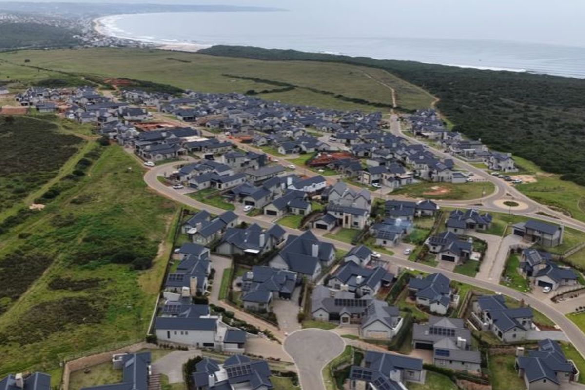 An aerial view of a residential estate situated along the coastline, showcasing the layout of homes, road infrastructure, and surrounding natural landscape.