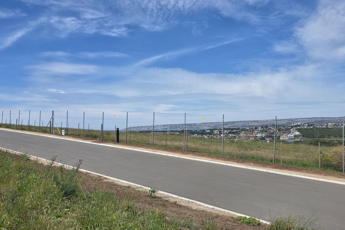 A view of a paved residential road with electric perimeter fencing, overlooking a coastal landscape and distant town.