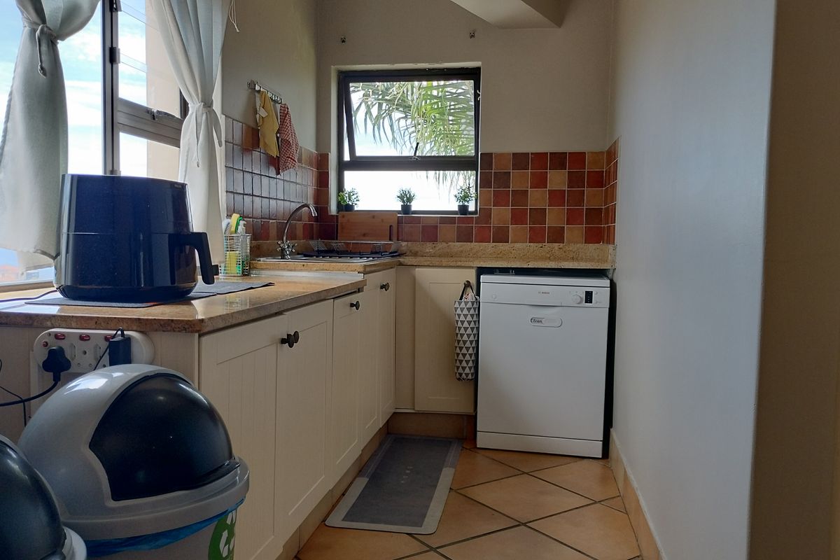A compact kitchen featuring built-in cabinetry, stone countertops, a tiled backsplash, and a functional layout with an integrated dishwasher.