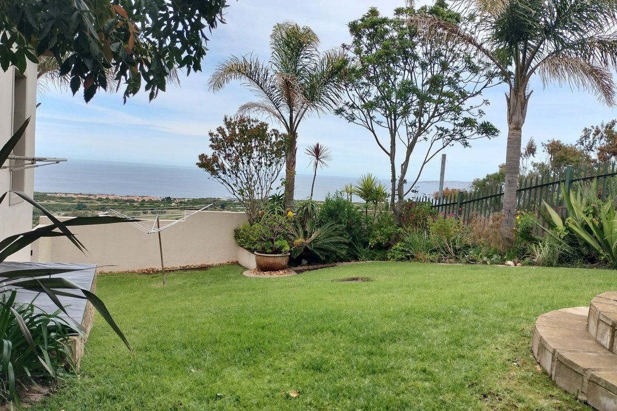 A well-maintained rear garden featuring a lawn, stone steps, and a retaining wall, offering scenic coastal views.