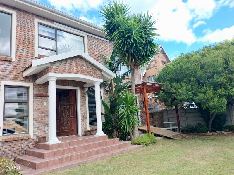 Front elevation of a face brick house featuring a covered entrance with decorative columns, tiled steps, and an adjacent timber pergola in the garden.