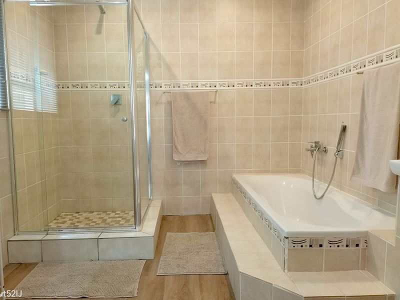 A functional bathroom featuring a glass-enclosed shower, a built-in bathtub with tiled surround, and neutral ceramic wall tiling.