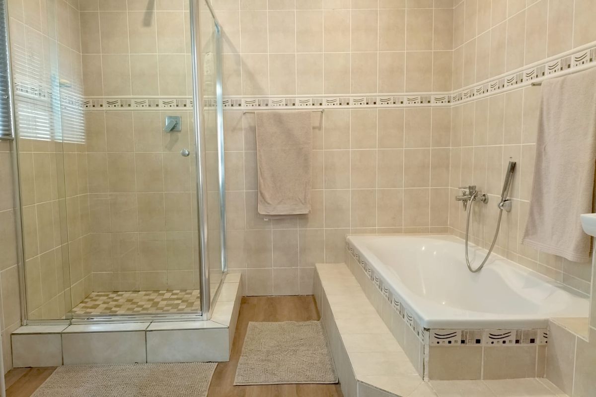 A functional bathroom featuring a glass-enclosed shower, a built-in bathtub with tiled surround, and neutral ceramic wall tiling.