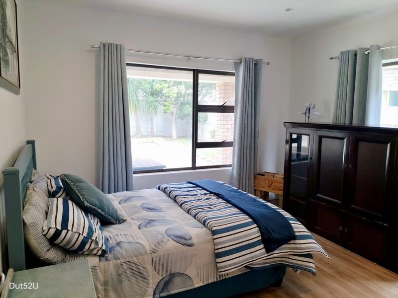 A well-maintained bedroom featuring laminate flooring, neutral walls, and a large window providing natural light and views of the rear garden.