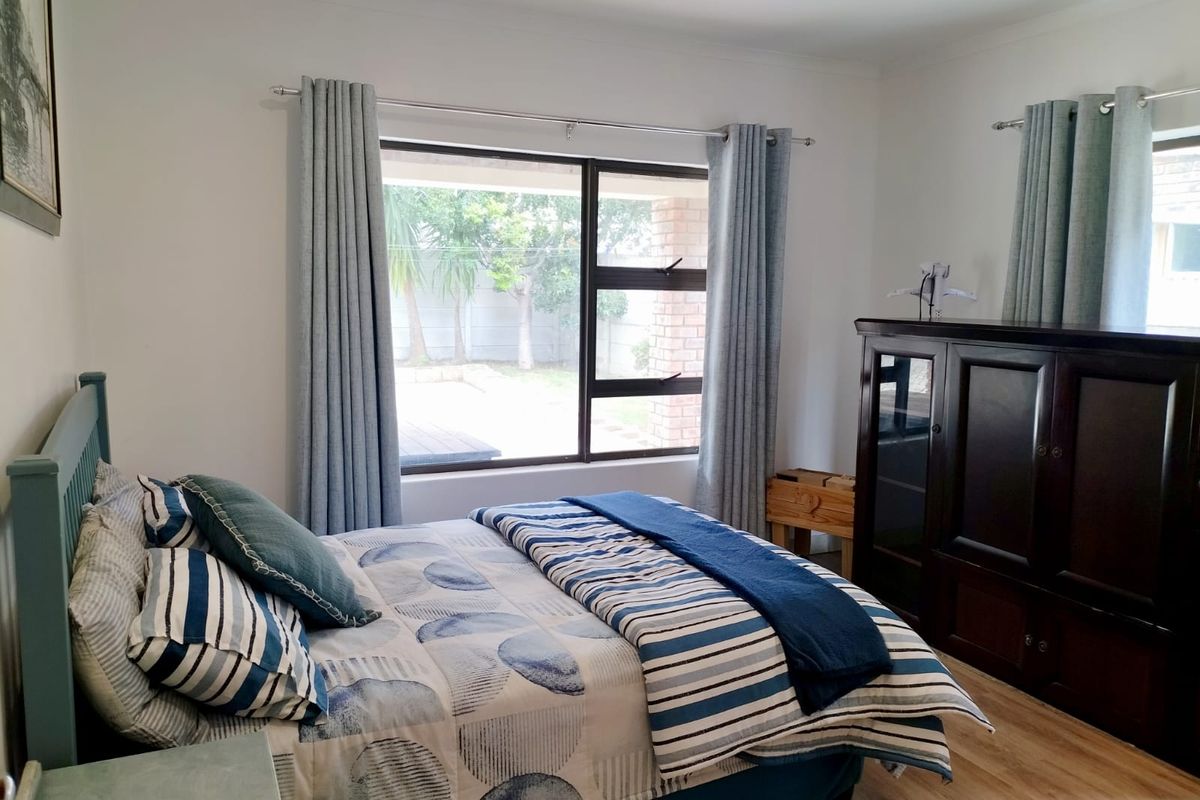 A well-maintained bedroom featuring laminate flooring, neutral walls, and a large window providing natural light and views of the rear garden.