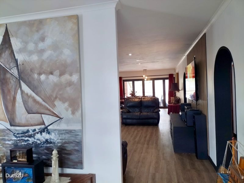 Spacious open-plan living area featuring timber-look flooring, a decorative slatted wall panel, and large sliding glass doors leading to the outdoor space.
