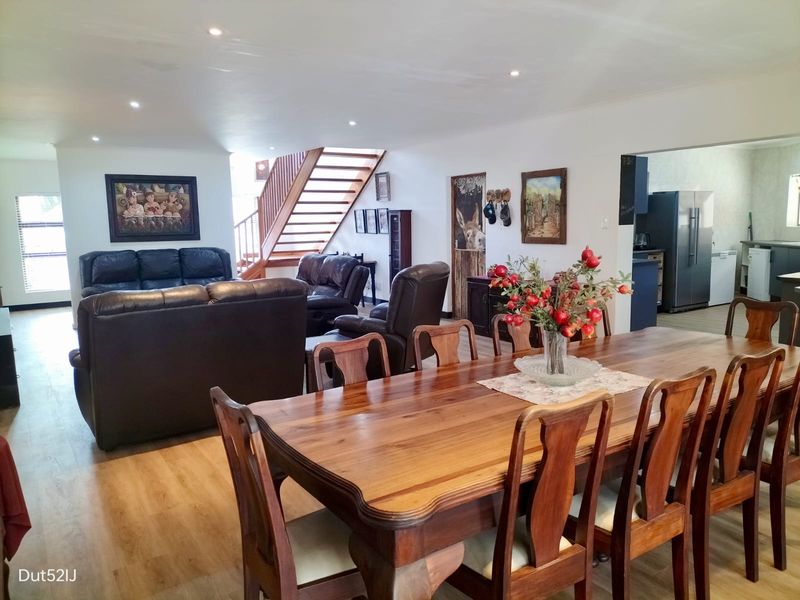 Spacious open-plan living and dining area featuring laminate flooring, recessed lighting, and a prominent wooden staircase leading to the upper level.
