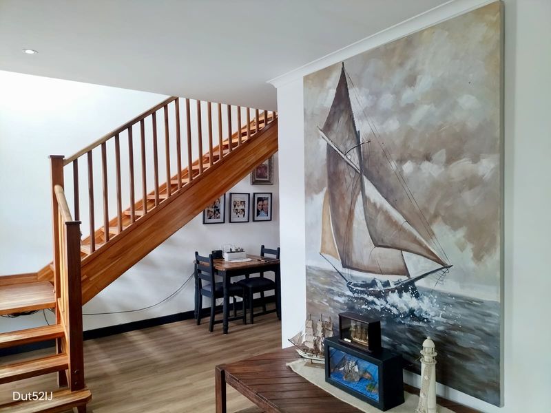 A bright hallway featuring a prominent timber staircase with matching balustrade and modern laminate flooring, creating a warm and inviting entrance area.