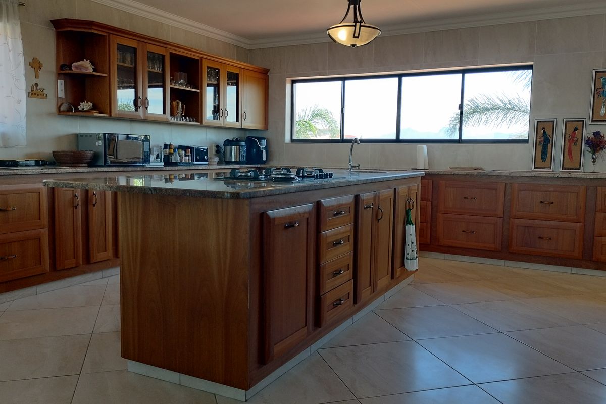 Spacious kitchen featuring warm wooden cabinetry, a large central island with a gas hob, granite countertops, and ample natural light from sliding windows.