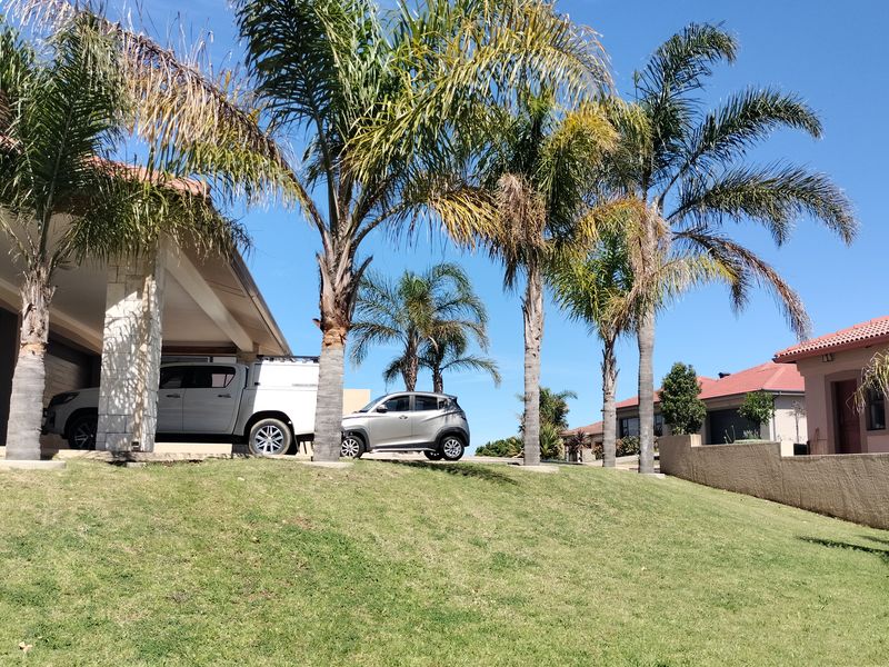 Front elevation of the property featuring a stone-clad pillar, tiled roof, and a well-maintained lawn with established palm trees.