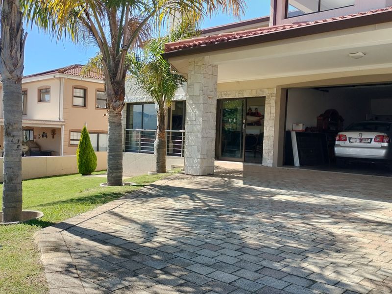 Front elevation of a modern house featuring a paved driveway, stone-clad pillar, and integrated double garage with a well-maintained garden.