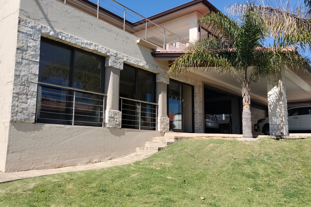Rear view of the property featuring stone cladding, sliding glass doors, a covered patio area, and an upper-level balcony with stainless steel railings.